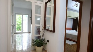 Un couloir avec une plante en pot, un miroir et une porte donnant sur une chambre où se trouve un lit superposé.