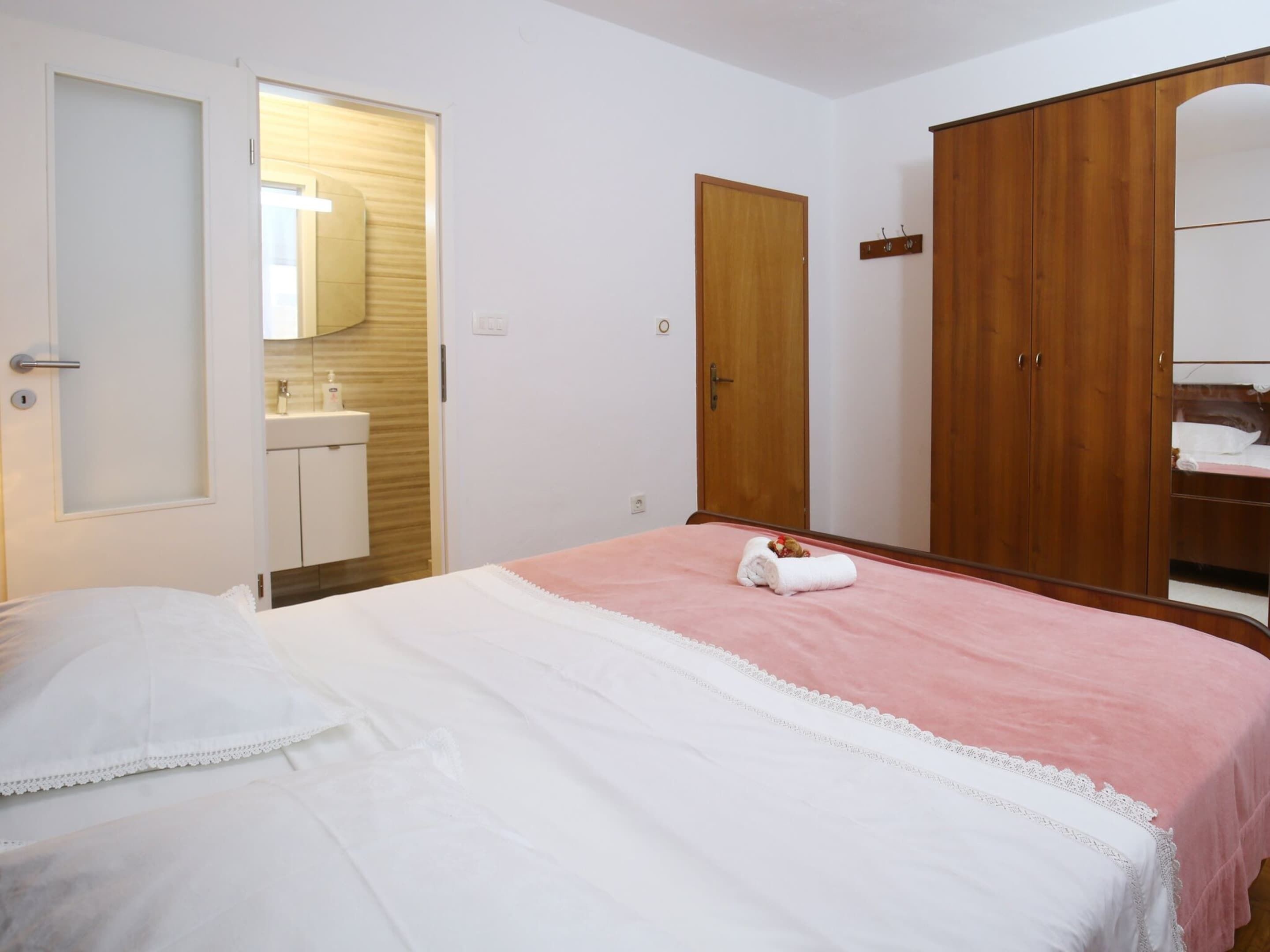 Une chambre à coucher comprenant un lit, une armoire en bois, un miroir et une salle de bain avec un lavabo.