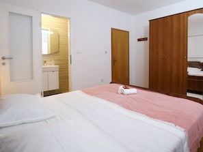 Een slaapkamer met een bed, een houten garderobe, een spiegel en een badkamer met een wastafel.