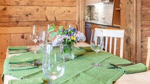 Ein Interieur einer Holzhütte mit einem für sechs Personen gedeckten Esstisch, einem grünen Tischläufer, Weingläsern und einer Vase mit Blumen.