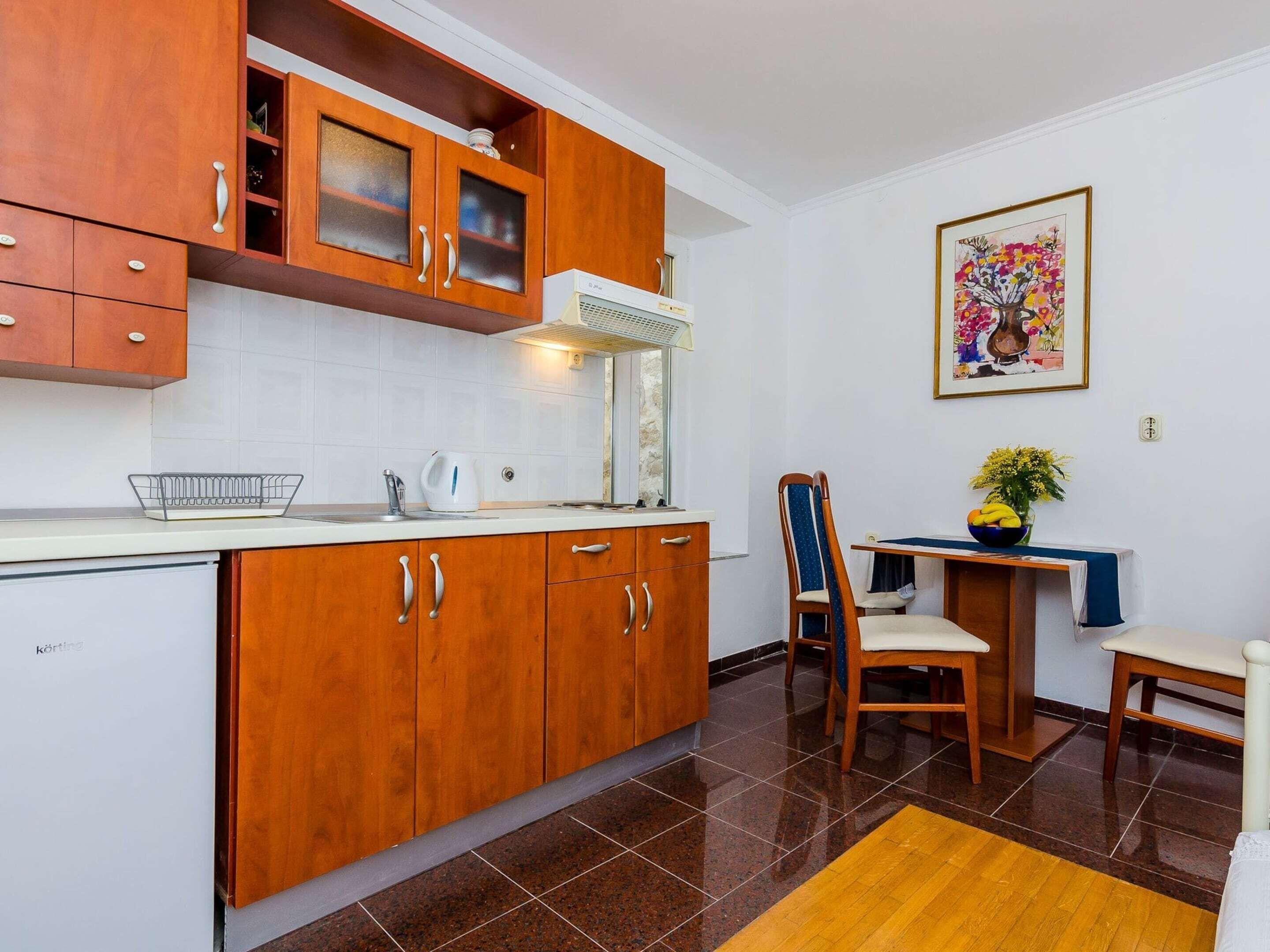 A compact kitchen with wooden cabinets, a white countertop, and a small dining area with a chair and table.