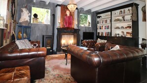 A cozy living room with leather sofas, a fireplace, a chandelier, and a bookshelf filled with books and decorative items. - Atelier House With hot tub (Sleen)