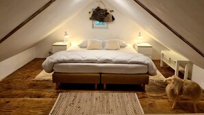 A bedroom with a sloped ceiling, a bed with white bedding, two bedside lamps, and a small rug on the wooden floor. - Atelier House With hot tub (Sleen)