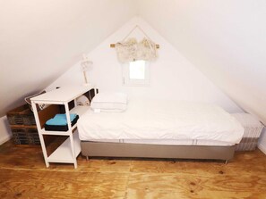 Ein kleines, dreieckiges Schlafzimmer im Dachgeschoss mit einem Bett, einem weißen Schreibtisch und einem kleinen Fenster.
