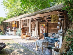 Ein rustikaler Außenbereich zum Sitzen mit einem Holztisch, Stühlen und einer Couch unter einem Reetdach.