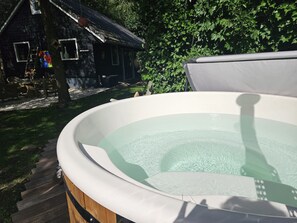 Ein Whirlpool im Freien mit einer Holzterrasse und einem rustikalen Haus im Hintergrund.