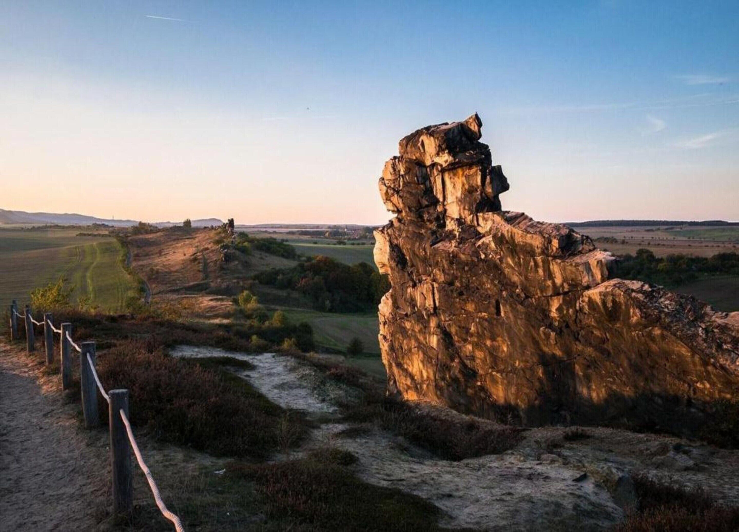 A natural rock formation with a fenced path leading to it.