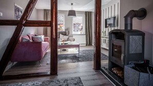 Ein gemütliches Wohnzimmer mit einer Holztreppe, einem Kamin, einem rosa Sofa und einem Fernseher.