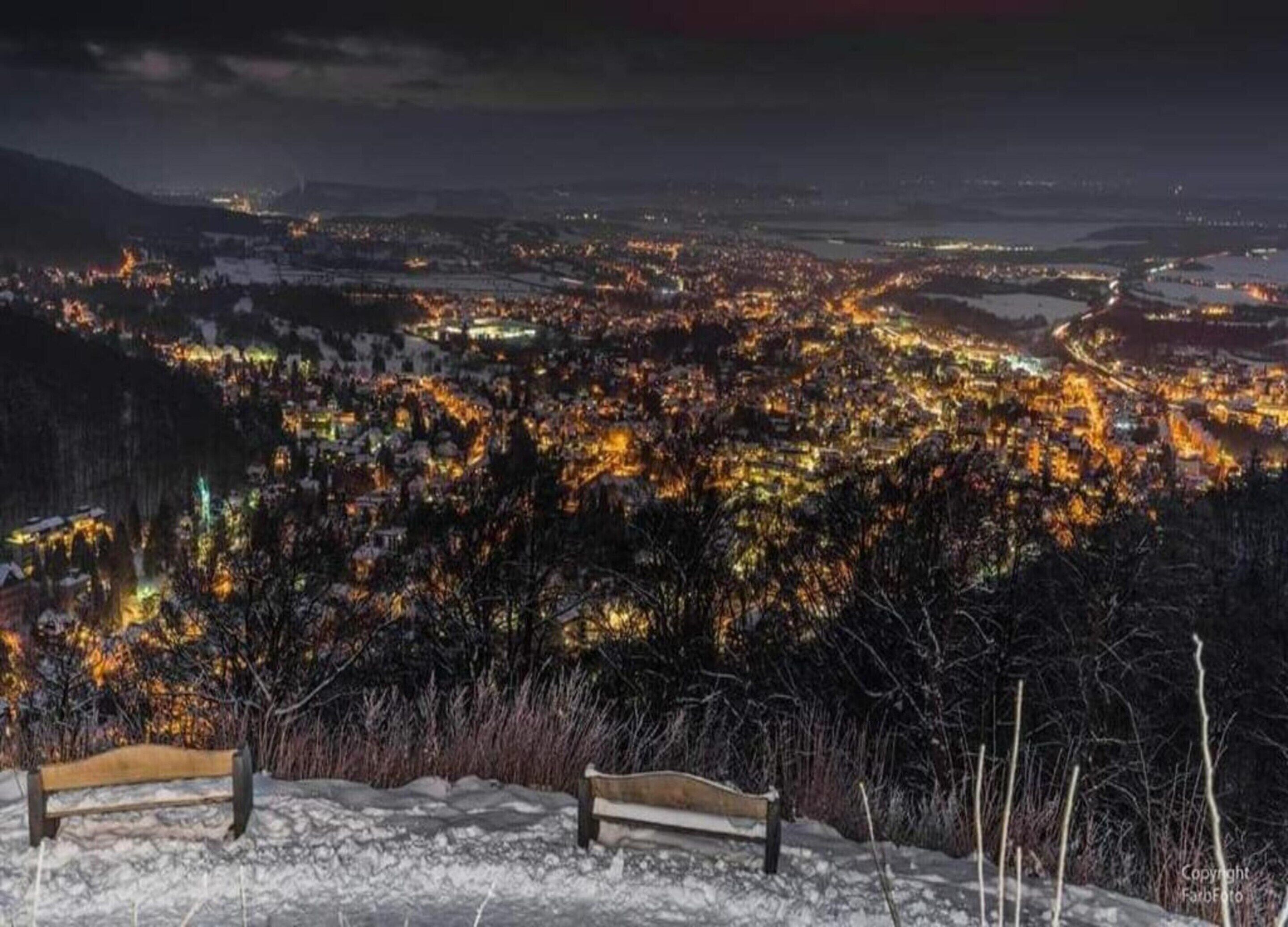Eine Bank mit Blick auf eine verschneite Landschaft, in der Ferne eine Stadt.