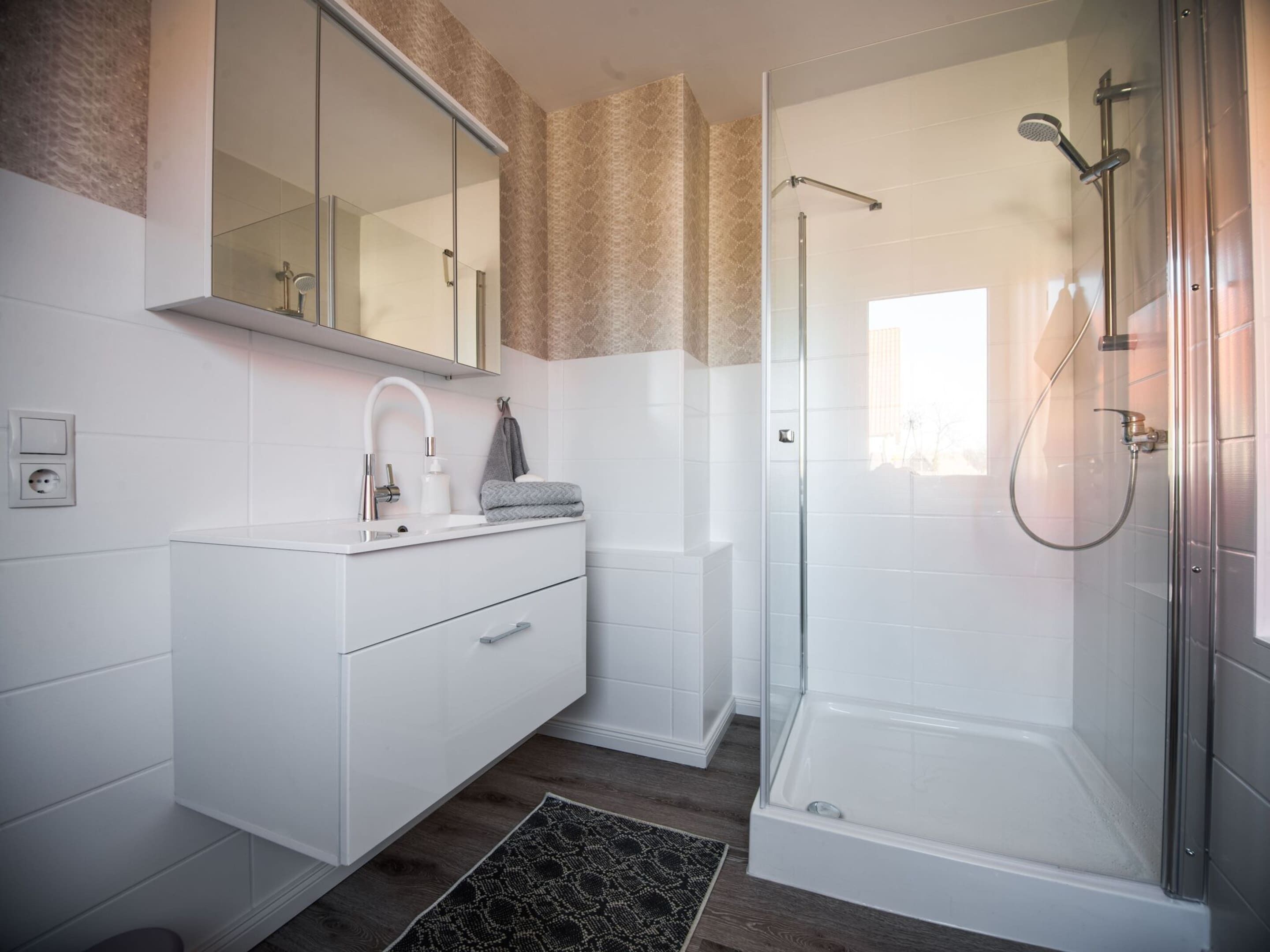 Une salle de bain moderne avec une douche à parois de verre, un meuble-lavabo blanc avec un miroir et un papier peint à motifs.