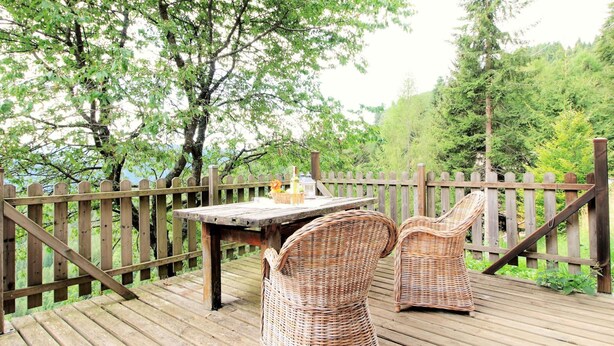 A wooden deck with wicker chairs and a table, surrounded by a wooden fence and trees. - Belvilla by OYO Hilltop Chalet in Lamon With Views (Lamon)