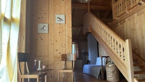A wooden interior with a staircase, a dining area with chairs, a table, and a bed in the background. - Belvilla by OYO Hilltop Chalet in Lamon With Views (Lamon)