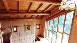 A wooden cabin interior with a sloped ceiling, multiple windows, and a staircase leading to an upper level. - Belvilla by OYO Hilltop Chalet in Lamon With Views (Lamon)