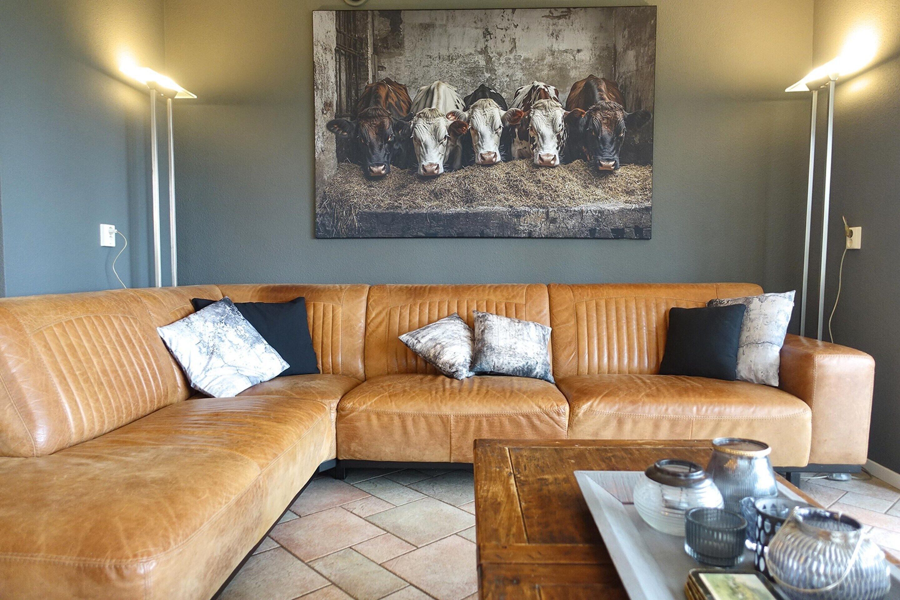 Una habitación con un sofá de cuero, una mesa de centro con objetos decorativos y un cuadro de vacas en la pared.