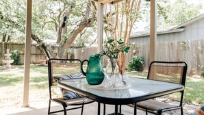 An outdoor patio with a glass table, two chairs, a green pitcher, and a vase with flowers. - 3BR/2BA Cozy Home - 10mins to the Domain, Q2 stadium, 15mins to Downtown Austin  (Austin)