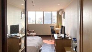 A hotel room with a bed, a desk with a computer, a chair, and a window with a city view. - Hermes Hotel (Hsinchu)