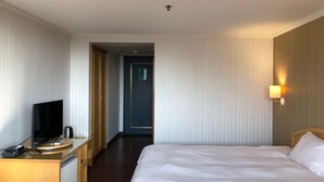 A hotel room with a bed, a desk with a television, and a wall-mounted lamp. - Hermes Hotel (Hsinchu)