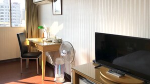 A hotel room with a bed, a desk with a lamp, a chair, a TV, and a fan. - Hermes Hotel (Hsinchu)