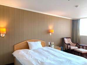 A hotel room with a bed, two wall-mounted lamps, a chair, and a small table. - Hermes Hotel (Hsinchu)