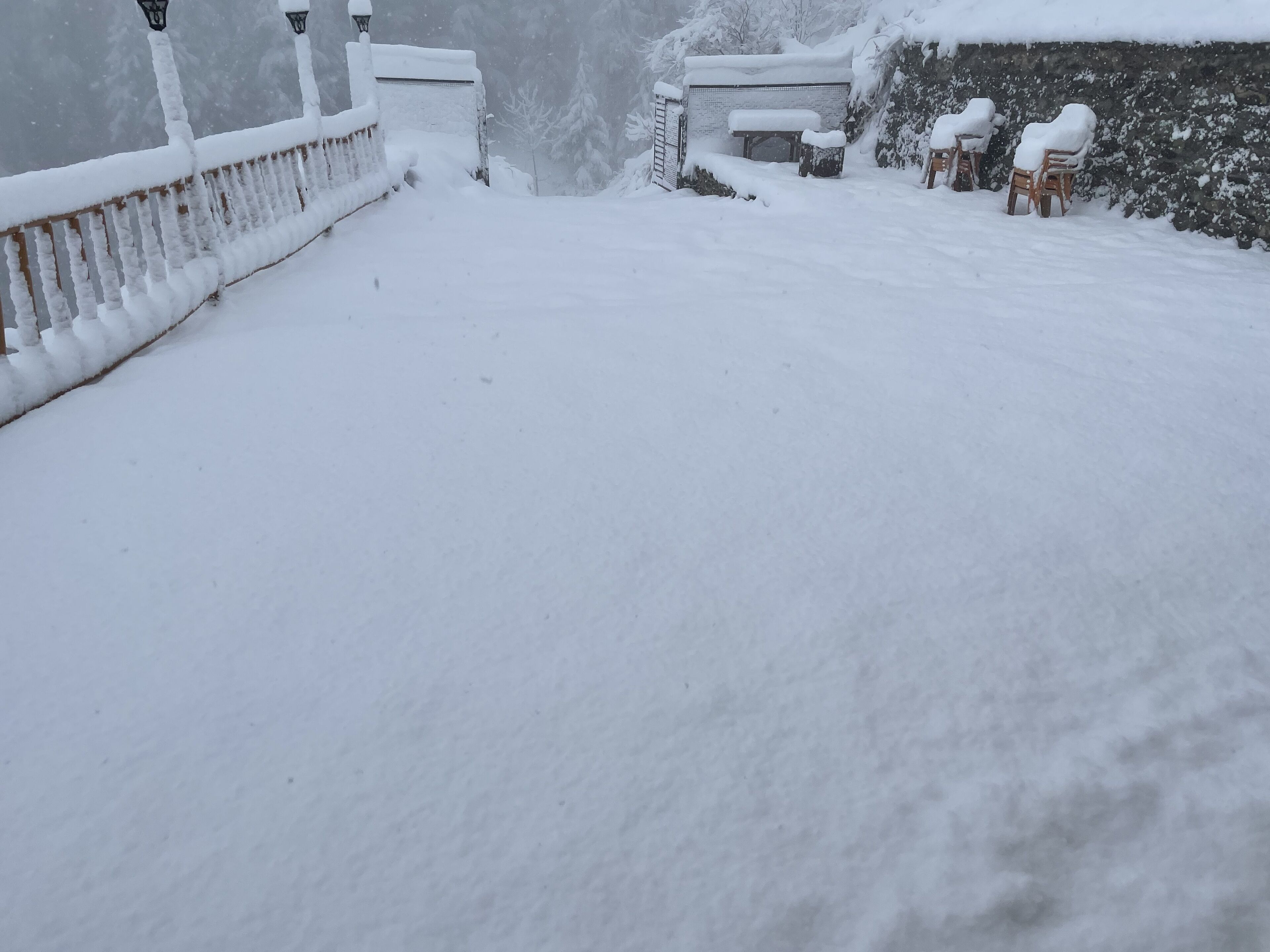 A snow-covered outdoor area with a wooden fence, a bench, and a small structure.