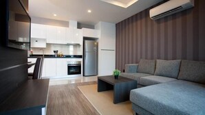 Eine moderne Küche mit weißen Schränken, einem eingebauten Backofen und einem Kühlschrank. Im Wohnbereich befindet sich ein graues Sofa und ein kleiner Couchtisch.