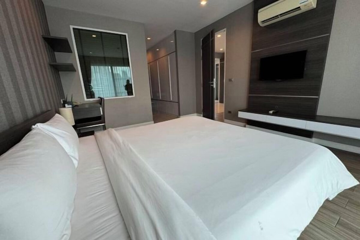 Una habitación de hotel moderna con una cama grande, un televisor montado en la pared y un armario empotrado.