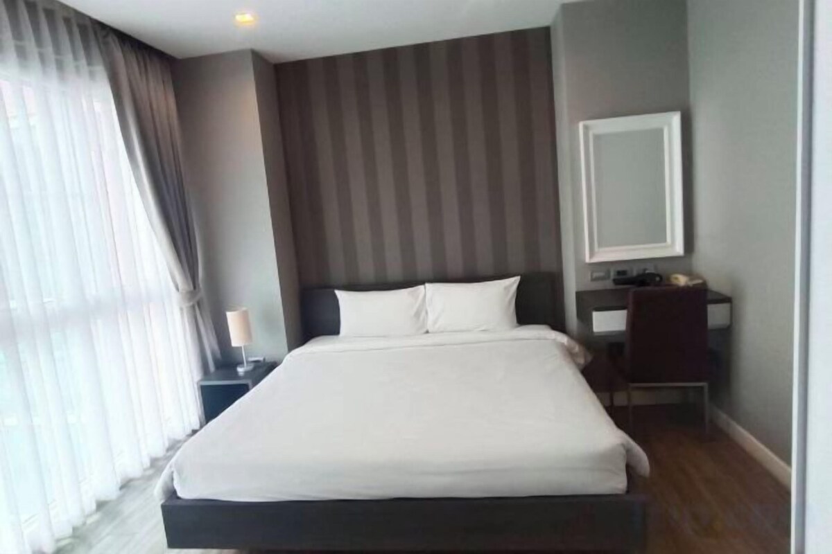 A hotel room with a large bed, a bedside table, a mirror, and a window with curtains.