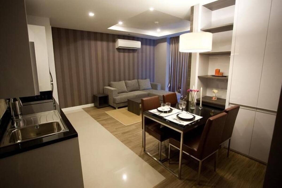 Una habitación de hotel moderna con kitchenette, zona de comedor, sofá y un ventanal grande.