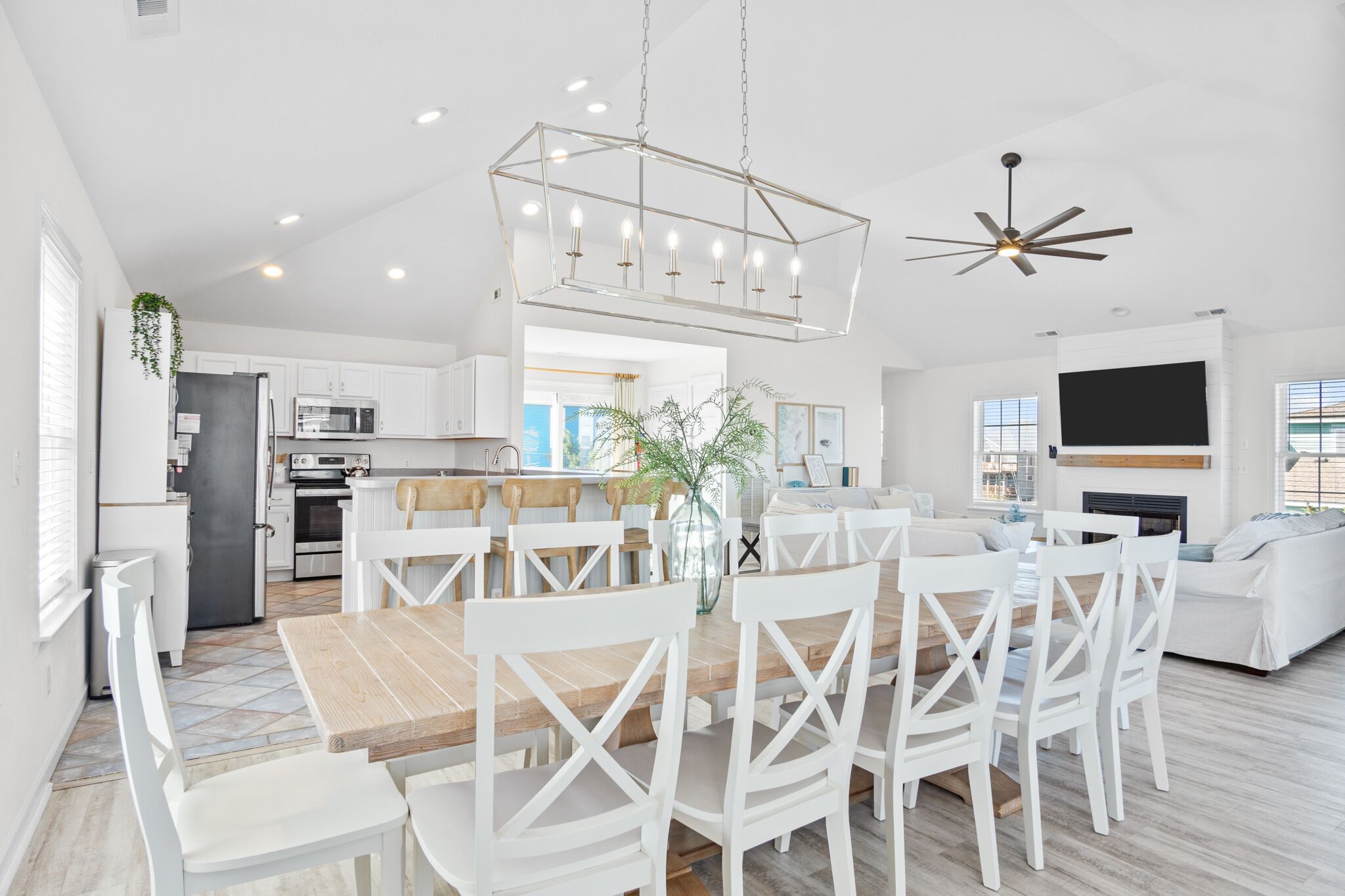 Une cuisine moderne avec des meubles blancs, un coin repas avec une table en bois et des chaises blanches, et un salon avec un canapé blanc et un téléviseur à écran plat.