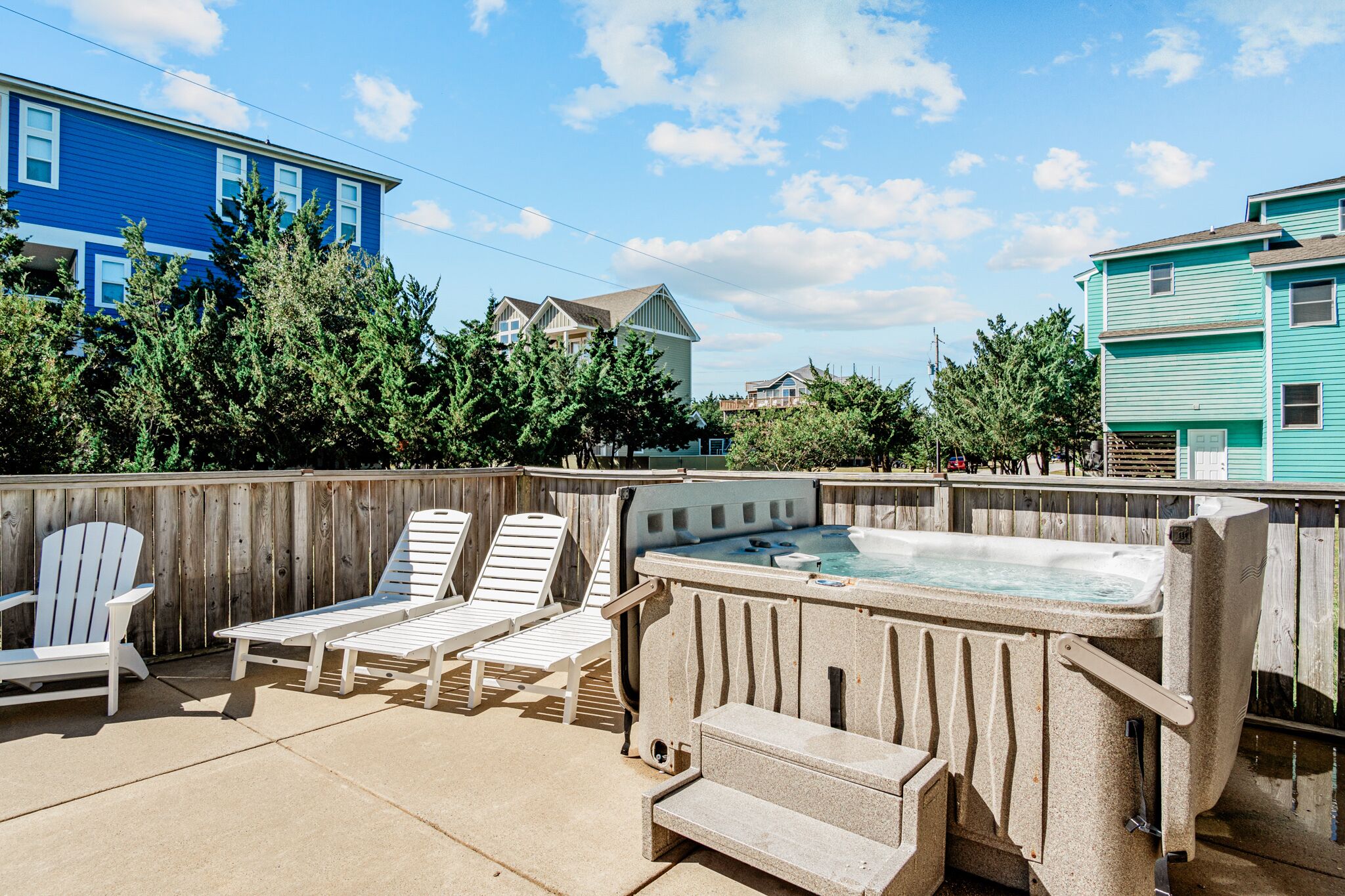 Un patio trasero con un jacuzzi, dos sillas Adirondack y una valla de madera.