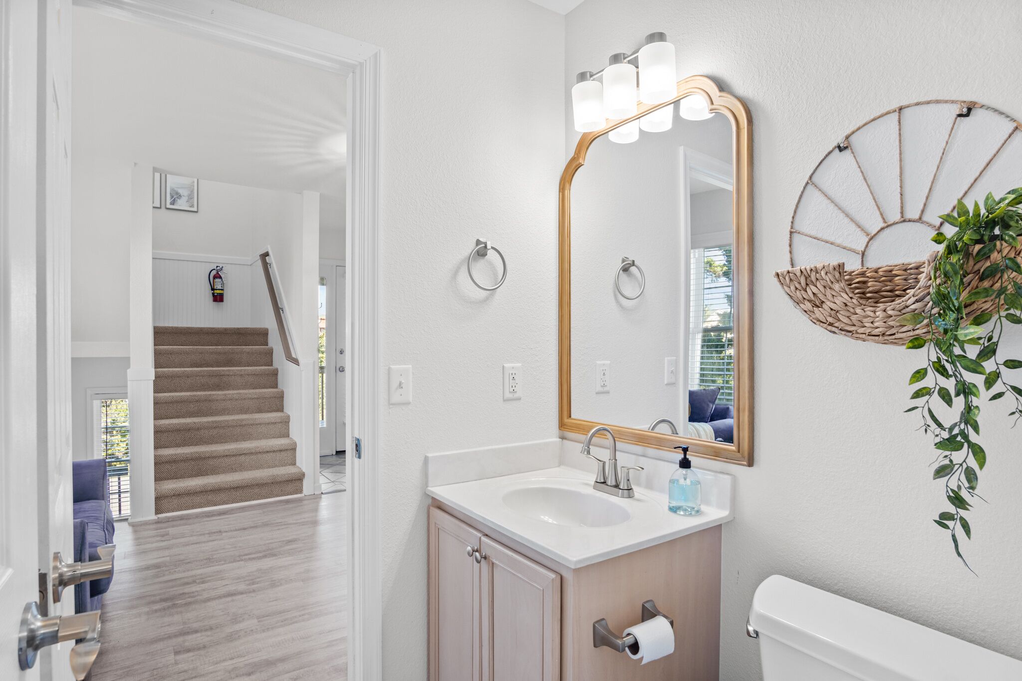 Un baño con un lavamanos blanco, un espejo con luces, un inodoro y una escalera que lleva a otra habitación.