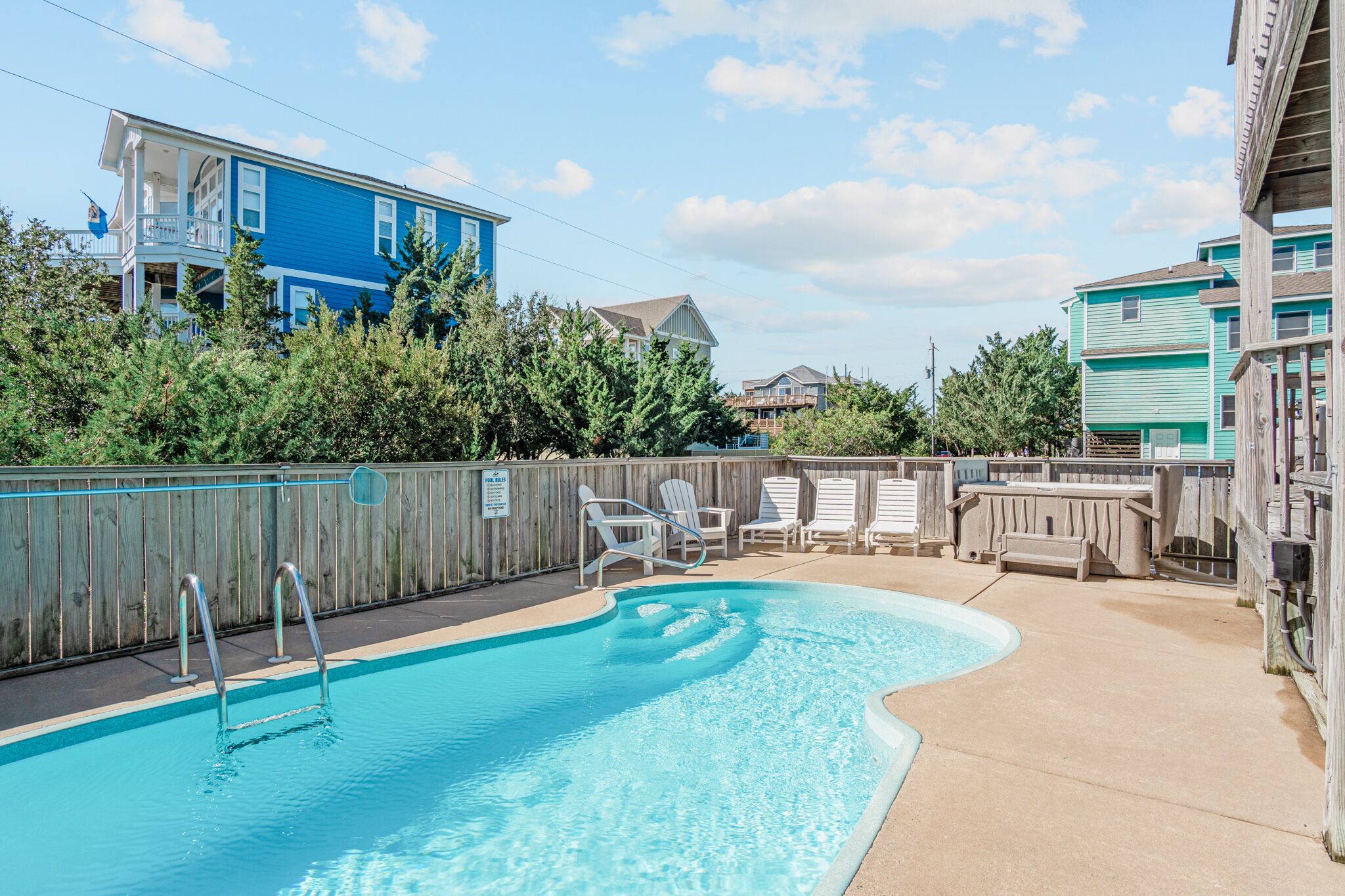 A swimming pool with a wooden deck and lounge chairs, surrounded by a wooden fence and trees.