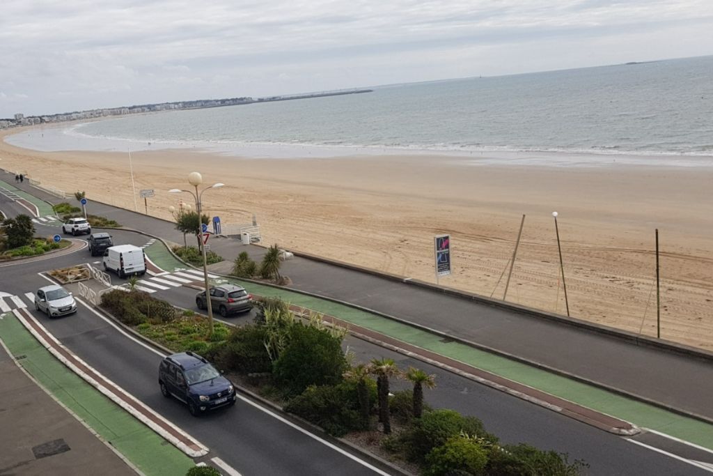 Una carretera costera con una playa a un lado y un carril bici verde al otro.