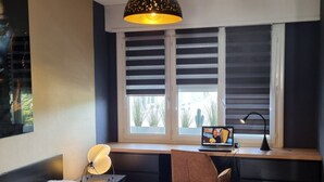 Ein Schlafzimmer mit Bett, Schreibtisch, Laptop und einem Fenster mit Jalousien.