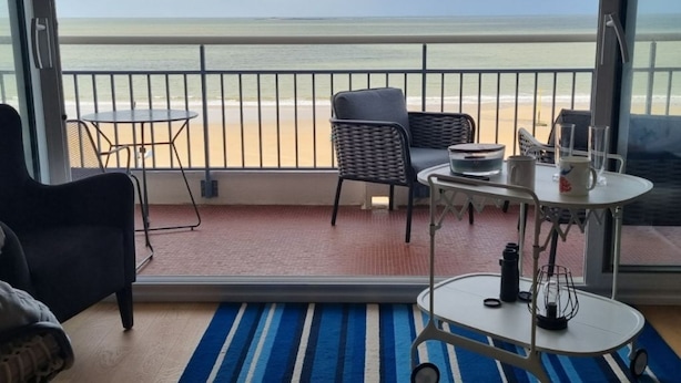 Ein Balkon mit Blick auf den Strand, ausgestattet mit einem Tisch, Stühlen und einer kleinen Matte.