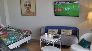 Ein Hotelzimmer mit einem Bett, einem Sofa, einem Sessel, einem kleinen Tisch mit Kerzen und einem Fernseher, der ein Fußballspiel zeigt.