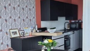 Eine moderne Küche mit schwarzen Schränken, einer schwarzen Arbeitsplatte und einem Essbereich mit einem runden Tisch und zwei Stühlen.