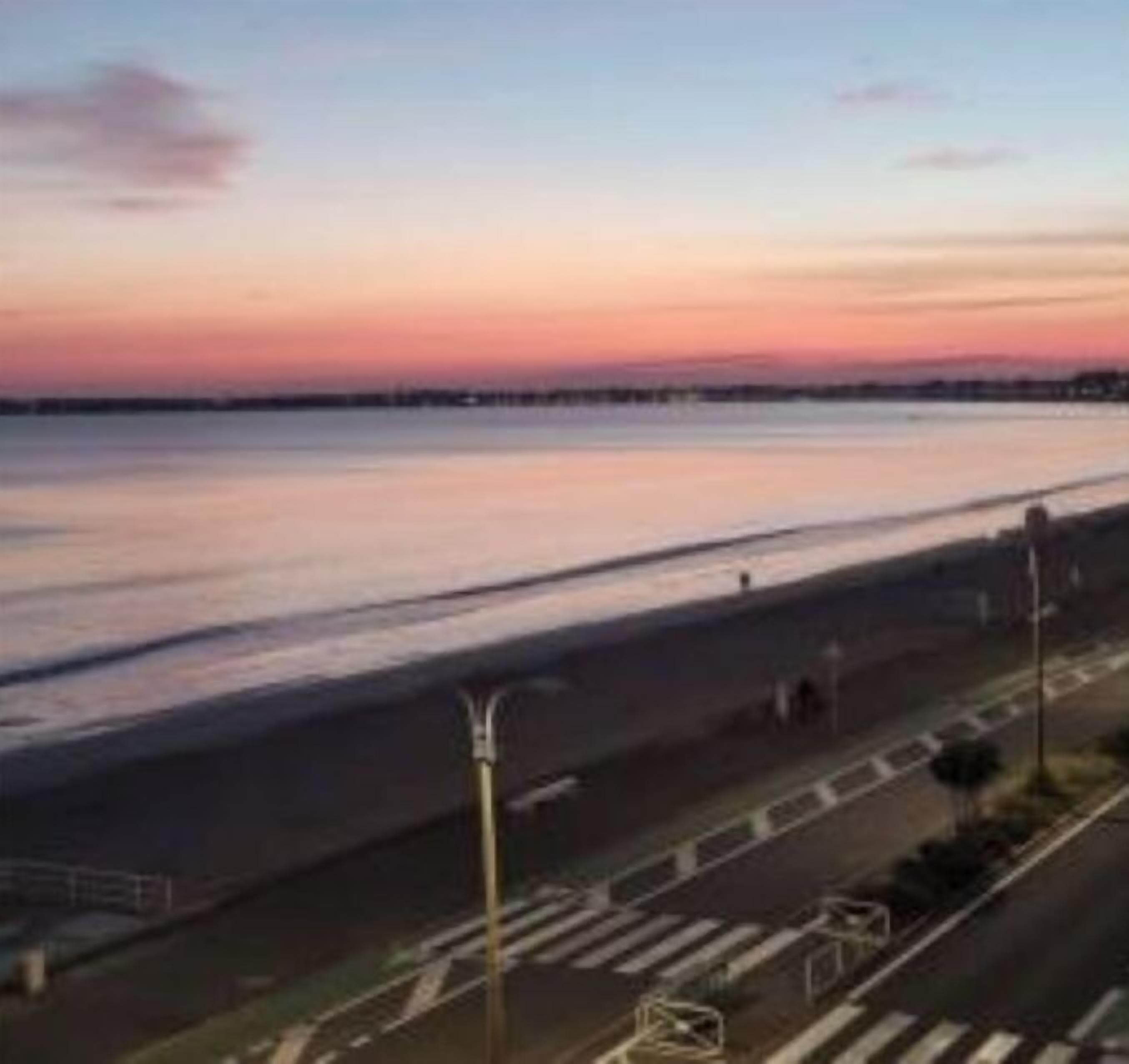 A coastal road with a pedestrian crossing and street lamps.