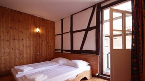 A room with a wooden bed, a window with a view, and a wall with a unique pattern. - Get-together in Fewo Holunder; celebrations with family and friends (Rosenthal)