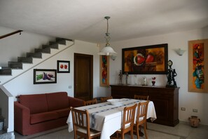 Een eetgedeelte met een tafel voor vier personen, een rode bank, een trap en verschillende kunstwerken aan de muur.