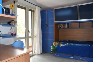 Een slaapkamer met een bed, een bureau en een stoel. Er is een raam met gordijnen, een boekenkast en een deur.