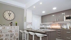 A modern kitchen with a central island, bar stools, a clock, and decorative tiles.