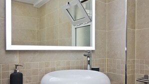A bathroom with a large mirror, a round white sink, and a shower.