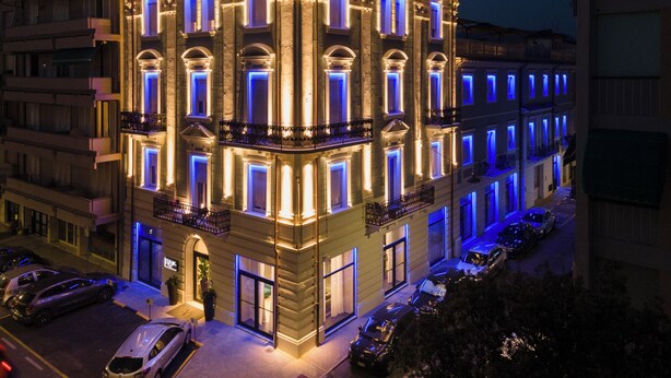A multi-story building with illuminated windows and balconies, parked cars in front, and a clear view of the street. - VI SUITES (Viareggio)