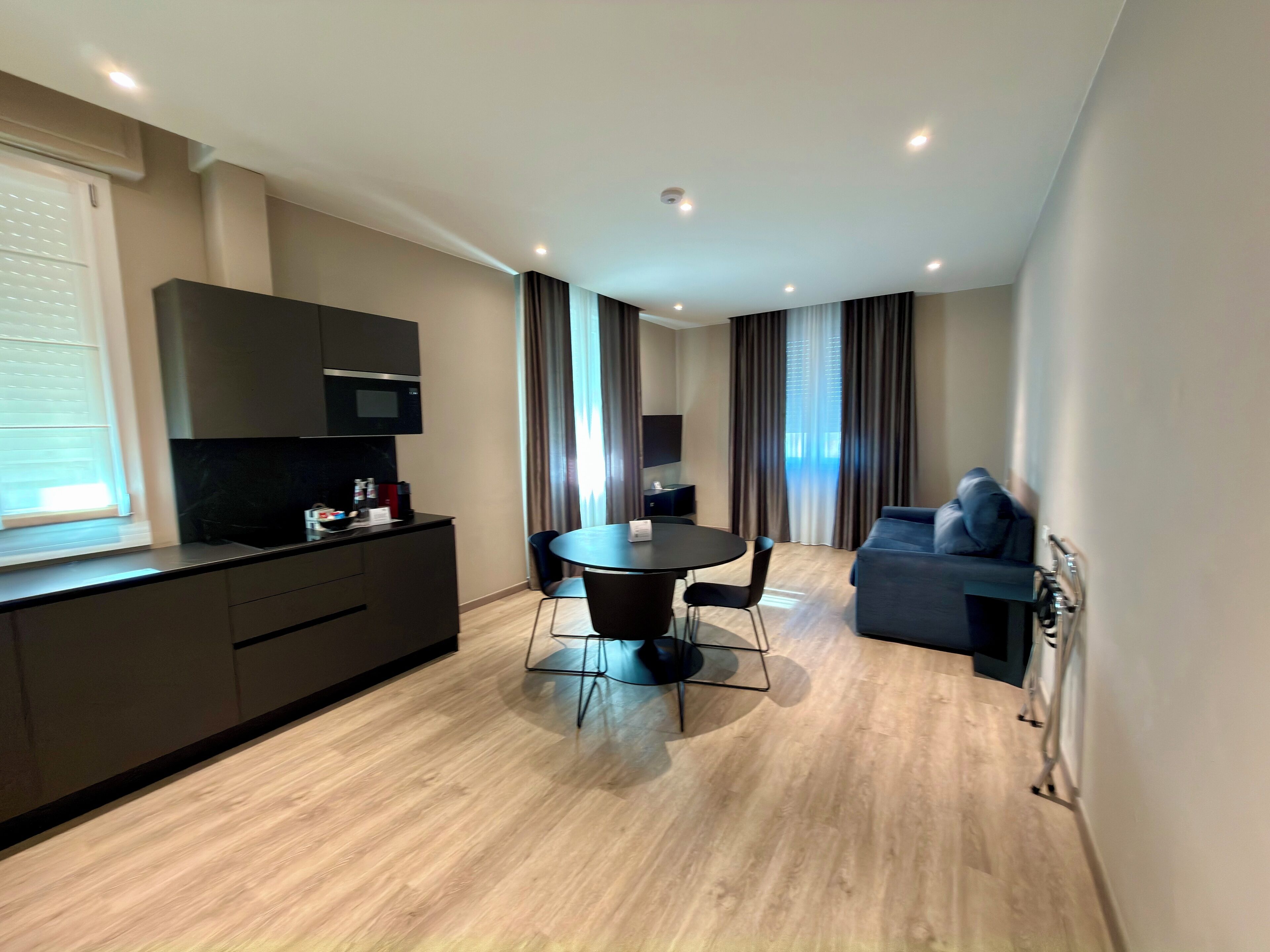 A modern hotel room with a kitchenette, a dining area, and a seating area.