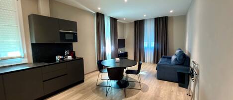 A modern hotel room with a kitchenette, a dining area, and a seating area.