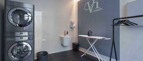 A modern laundry room with a front-loading washing machine, a sink, and an ironing station.