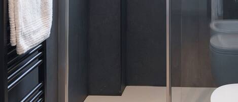 A modern bathroom with a glass shower enclosure, a white toilet, and a towel rack with towels.