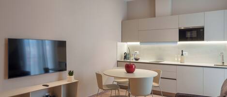 Una cocina moderna con un televisor de pantalla plana, una mesa de comedor con sillas y un microondas empotrado.