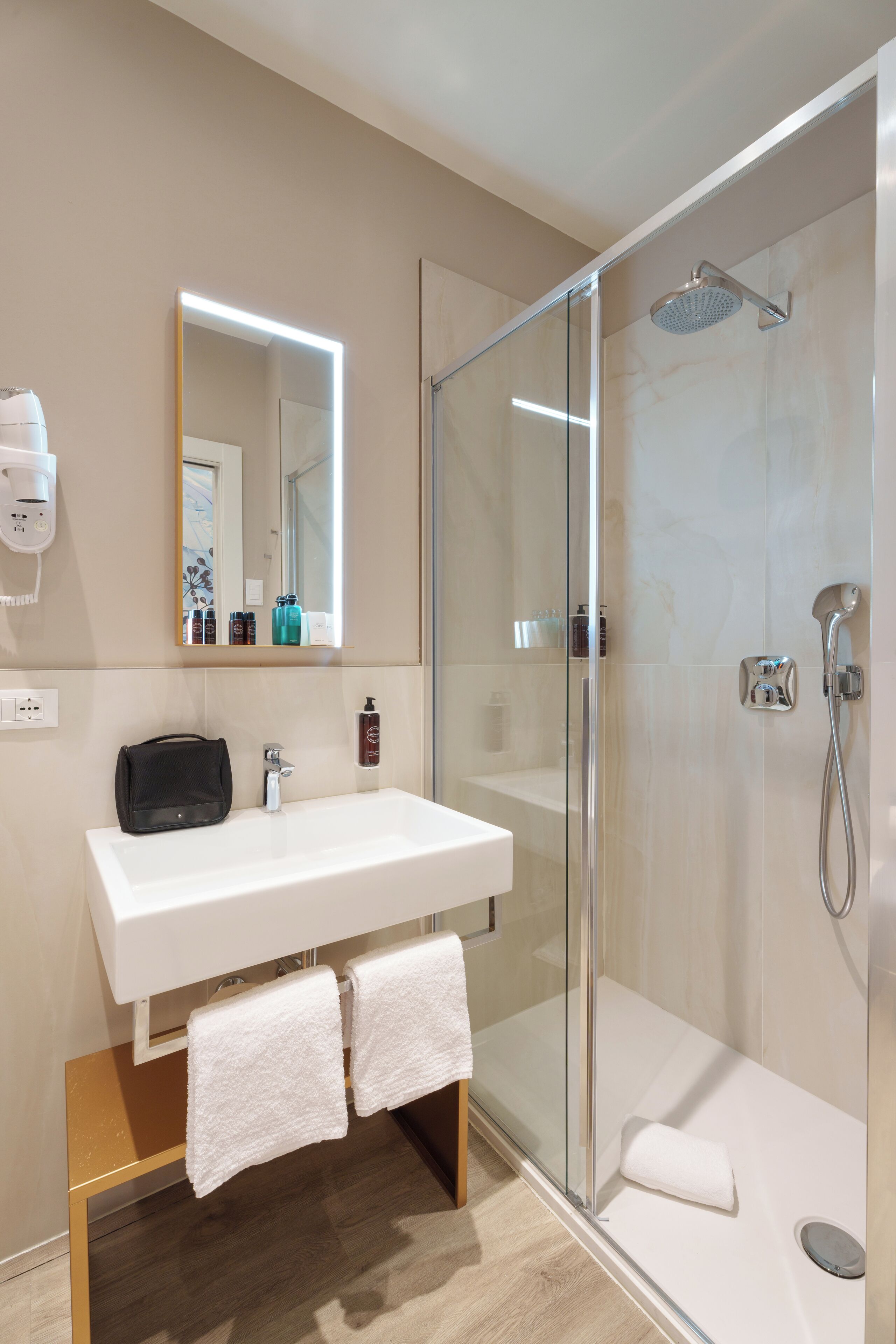 A modern bathroom with a glass-enclosed shower, a white sink, and a mirror with built-in lighting.